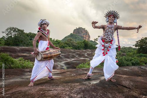 SIGIRIYA, SRI LANKA - DECEMBER 04, 2025 : A Gatabera Player (Getaberakaruwo) and a Ves Dancer or Up Country Dancer perform in front of Sigiriya Rock in Sri Lanka.