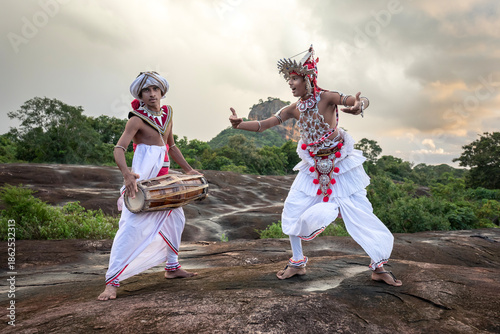 SIGIRIYA, SRI LANKA - DECEMBER 04, 2025 : A Gatabera Player (Getaberakaruwo) and a Ves Dancer or Up Country Dancer perform in front of Sigiriya Rock in Sri Lanka.