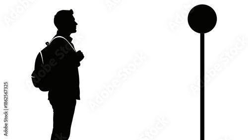 Silhouette of a male student or traveler wearing a backpack standing patiently while waiting near a simple vertical signpost in bright isolation