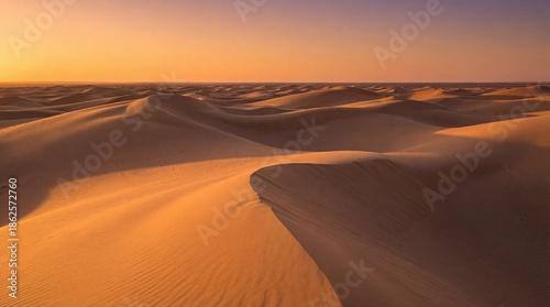 A stunning minimalist landscape featuring vast, rolling sand dunes stretching endlessly toward the horizon. The scene is bathed in warm golden hour light during sunset, creating deep, dramatic shadows