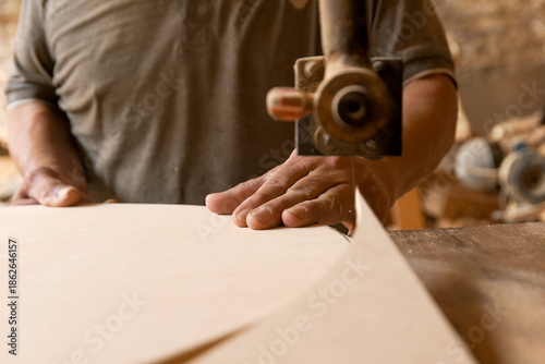 Carpenter cutting wood with industrial saw, hands of craftsman in woodworking process