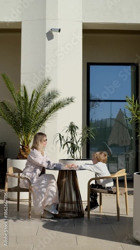 Woman and child engaging at outdoor table with plants and sunlight in view