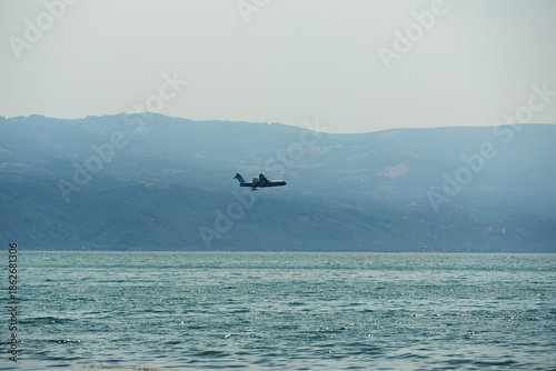 Water bomber flying over the sea with a mountain landscape. Aviation concept featuring a plane in flight over water and nature.