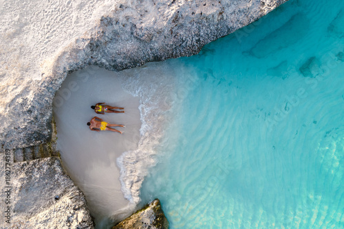 Two people unwind on the soft sands of Tres Trapi Beach in Noord, Aruba. With crystal-clear waters, this beautiful spot offers a perfect setting for relaxation and island exploration.