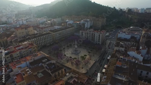 Drone advances above Malaga toward Plaza de la Merced and its central monument.