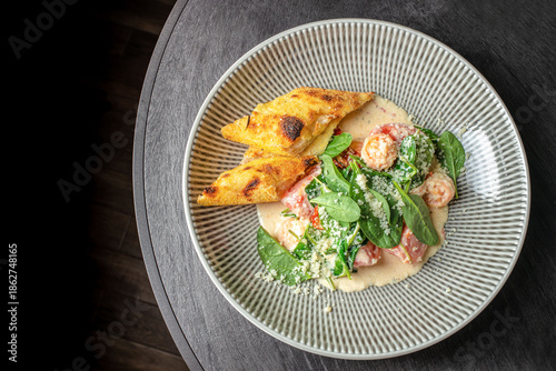 Shrimp with creamy sauce, fresh spinach and toasted bread served on plate, top view