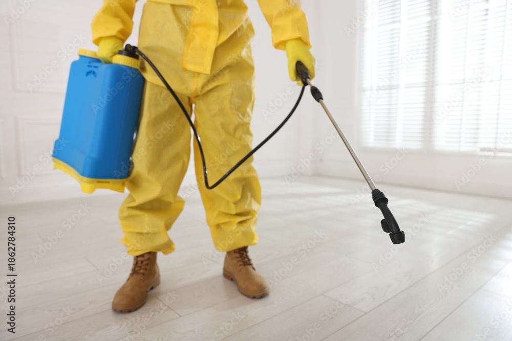 Fototapeta premium Pest control worker in protective suit spraying insecticide indoors, closeup