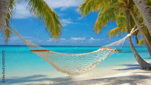 A hammock hangs between palm trees on a sandy beach by the ocean