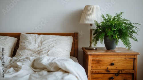 Serene minimalist bedroom with plush white duvet, wooden nightstand, lush green fern, soft lighting, and calming neutral tones radiating modern simplicity and tranquility