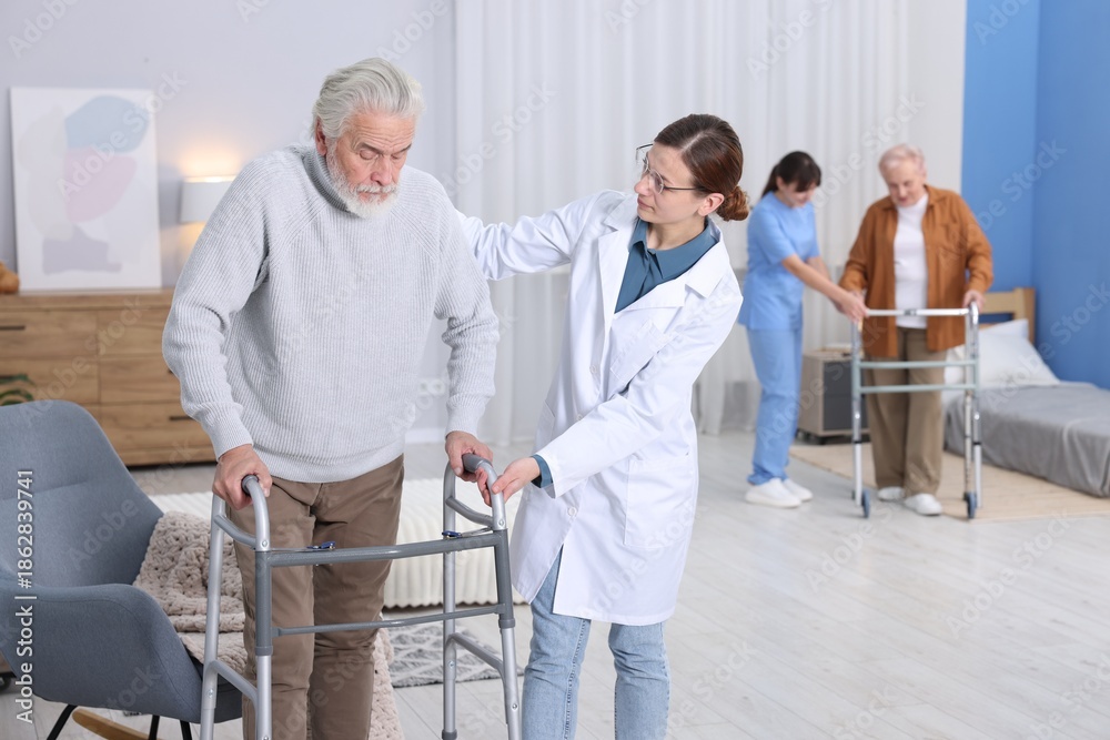 Fototapeta premium Care workers helping man and woman with walkers at retirement home, selective focus
