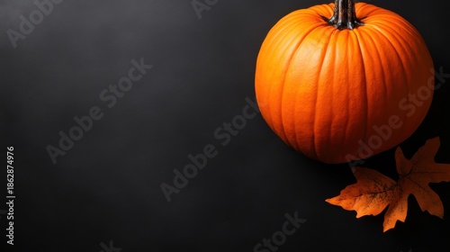 A vibrant orange pumpkin resting on a dark background accompanied by a bright autumn leaf, symbolizing the harvest season and Halloween festivities in a stunning display.