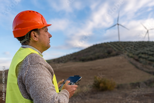 Tableau sur toile Worker in safety gear remotely controlling a drone against a backdrop of wind tu