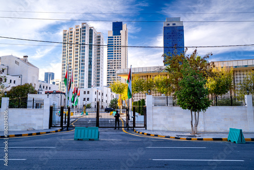 Tableau sur toile Gate with flags at the entrance to Jordanian Parliament, capital with modern skyscrapers in Amman