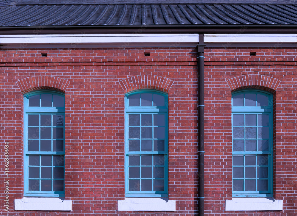 Fototapeta premium Red Brick Building Facade with Three Turquoise Windows For branding,calendar,postcard,screensaver,wallpaper,poster,banner,cover,website.High quality photo