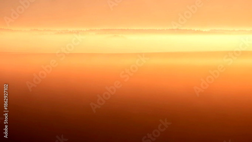 A serene landscape at sunset viewed from above with vibrant colors transitioning from orange to dark tones