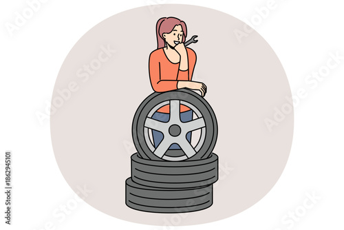 Woman auto mechanic prepares to replace car wheels during vehicle maintenance or repair. Happy girl auto mechanic with wrench in hands leans on tires, rejoicing at possibility replacing them on own