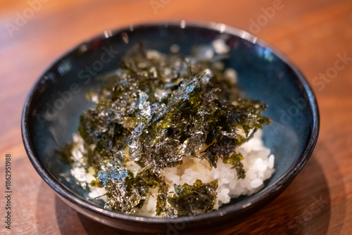A bowl of rice with seaweed served on the table