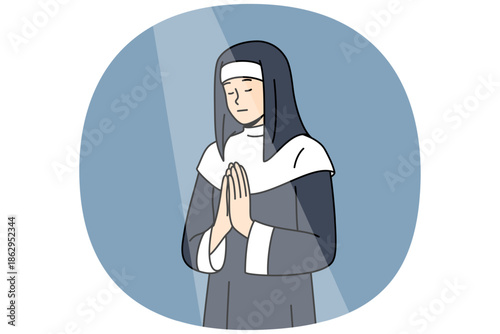 Nun prays to god with palms folded in front chest and eyes closed during ritual, standing under beam light in cathedral. Female novice catholic cathedral praying to observe christian traditions