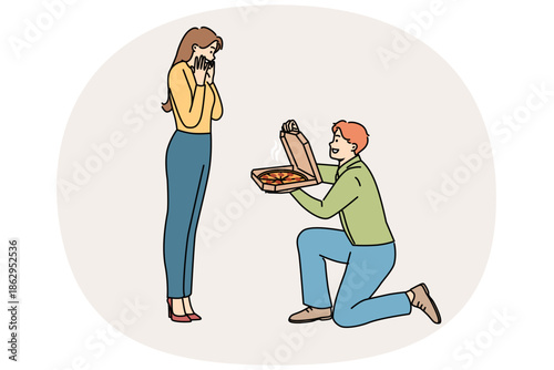 Man gives pizza to beloved, standing on knee and delighting girlfriend with fresh food from italian restaurant. Cheerful boyfriend proposes marriage to girl, with pizza instead of wedding ring