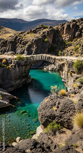 Historic stone arch structure spans a vibrant turquoise canyon river surrounded by rugged terrain
