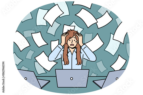 Overworked woman suffers from overload and clutches head sitting at table with laptops, among flying documents. Overworked secretary girl experiences stress and panic seeing volume of paperwork