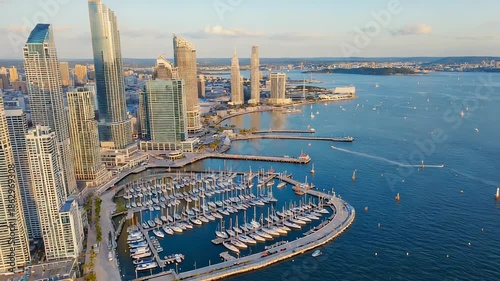 Aerial view of a luxury marina with numerous yachts and sailboats docked, showcasing a vibrant coastal lifestyle and upscale waterfront community.