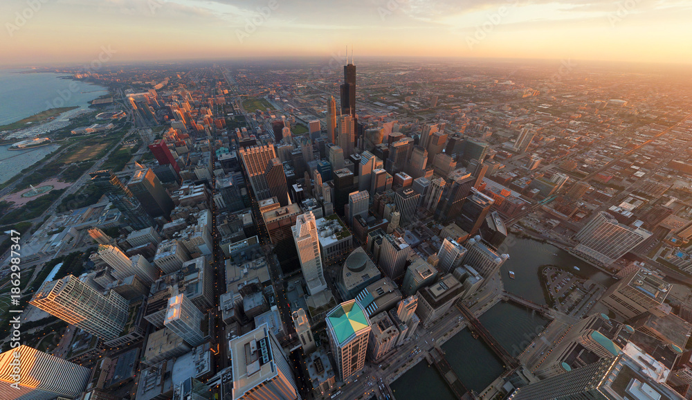 Aerial view of a sprawling cityscape, where the iconic Willis Tower pierces the skyline amidst the warm glow of the setting sun, Chicago, Illinois, United States.