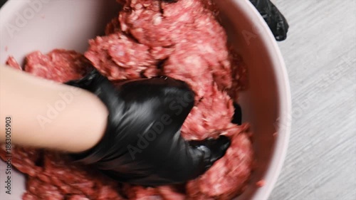 Top view hand of a chef in a black glove kneads and mixes red beef mince with salt and spices. Manual preparation of minced meat in an Islamic restaurant. Halal food with no pork content.