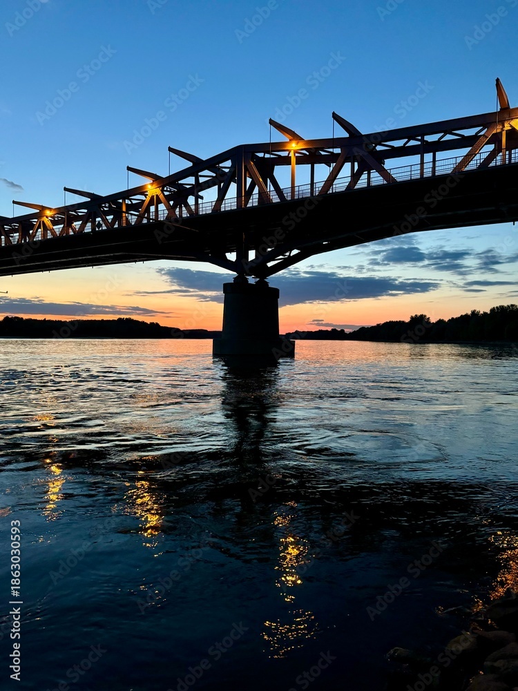 Fototapeta premium Bridge over a calm river at sunset with reflections.