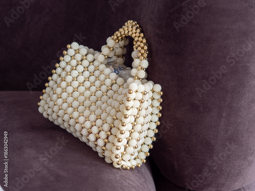 Foto An elegant, high-end bridal evening bag featuring intricate white pearls and gold beadwork, resting on a plush dark purple velvet sofa