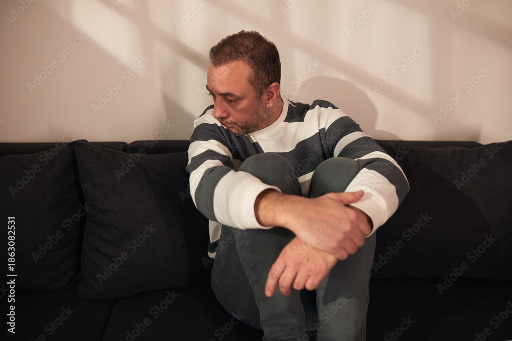 Obraz premium Man with headache, depression, sadness and loneliness sitting on a couch at home.