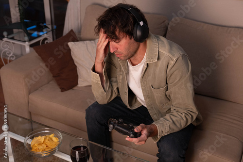 Fotografia Stressed man gaming late at night, feeling defeated and experiencing a headache,