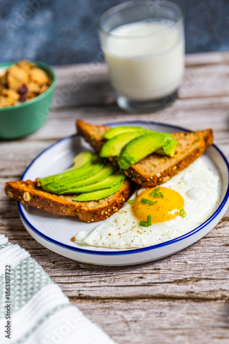 Healthy avocado toast with fried egg on rustic breakfast plate