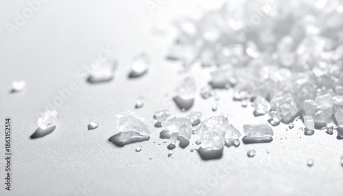 Extreme macro close up of large coarse translucent white crystals likely sea salt or rock salt scattered across a light textured gray background emphasizing cooking flavor and texture