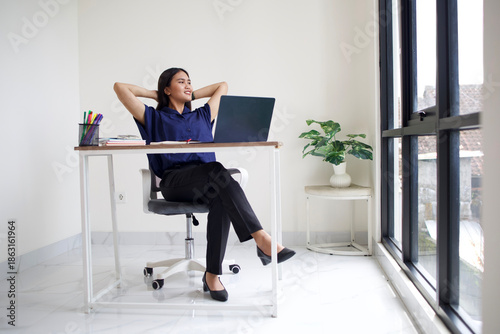 Relaxed Asian business woman take break from work put hands behind head lean on comfy chair, enjoy fresh conditioned air in modern office, no stress, fatigue relieve at workplace concept