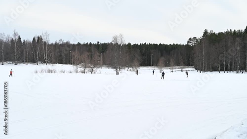 Group of people skiing on track in cross country ski zone during the winter. Ski track through the through woods with nature background on cloudy day.