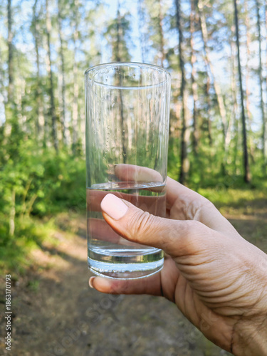 a man holds a glass of clear water in his hand against the backdrop of a forest,