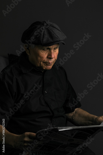 Foto An elderly man in dark clothing and a cap is sitting and reading a newspaper, looking at the camera with a gentle smile