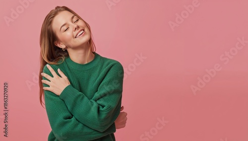 Woman Smiles While Hugging Herself in Front of a Pink Background During a Ind...