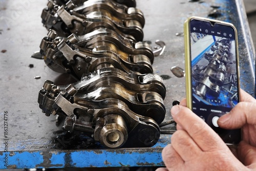 The camshaft and valve train components of a car engine. Mechanics inspect and document metal engine components. An engine mechanism on a work bench in a workshop during professional auto repair.