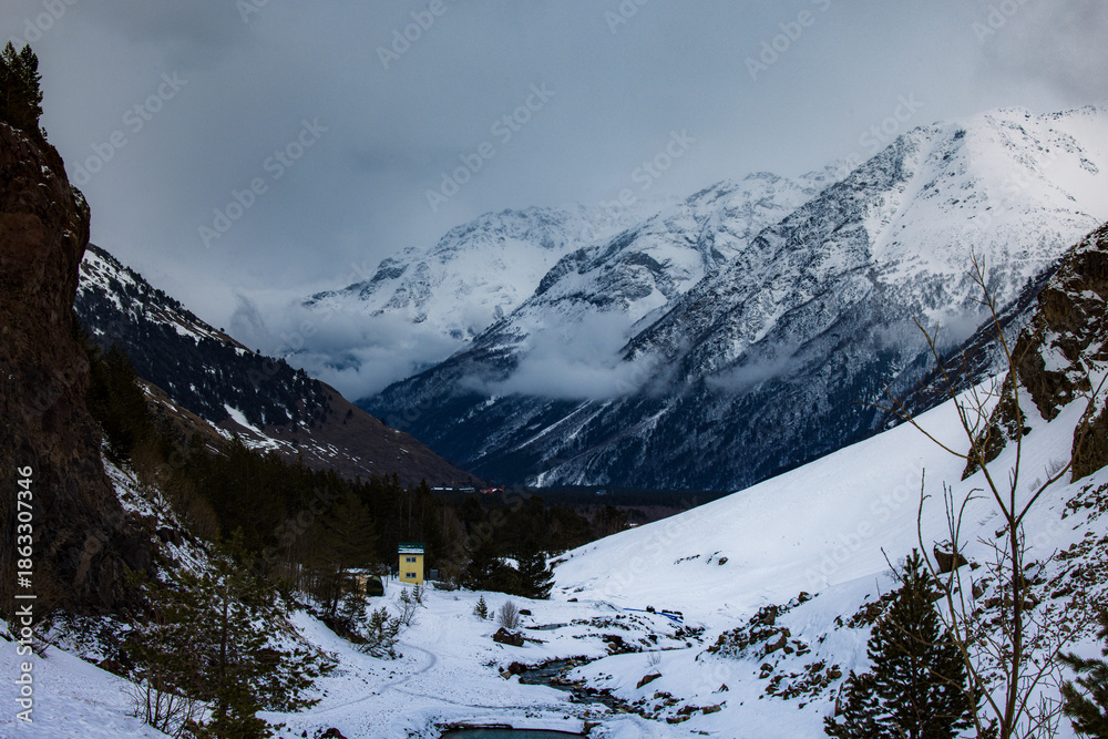 Naklejka premium Snowy Mountain Valley with River, Forest and Cloudy Sky