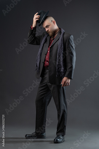 A man dressed in a noir style suit with elements of nonchalance and ethnic style, a charismatic man in a suit and hat in a photo studio on a gray background