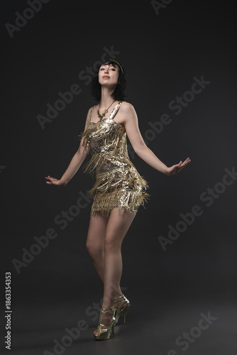 Flapper era femme fatale in short gold dress, Art Deco jewelry and bob. Dancing