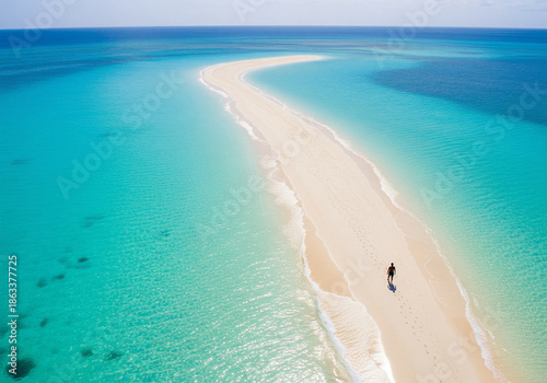 Coastline aerial photograph of aquamarine ocean and man walking along white sandbar beach