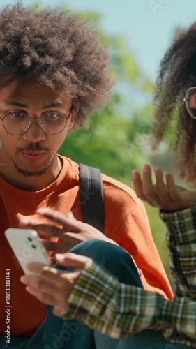 Confused African American students looking mobile phone discussing news outdoors surprising friends woman girl female education man male guy amazed wonder shock talk city friendship university college