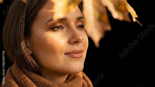 Young woman enjoying autumn sun with closed eyes and golden leaves.
