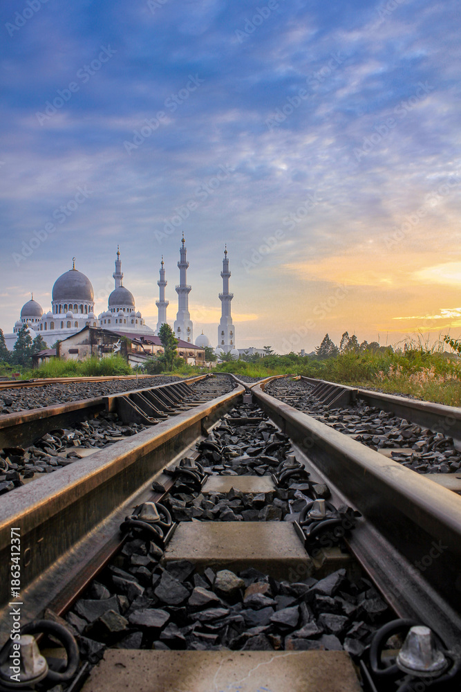 Obraz premium Architectural Grandeur of Mosque Towers Over Intersecting Railway Tracks at sunrise