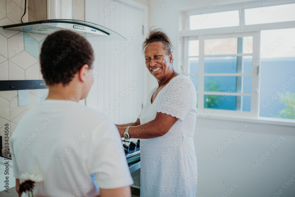 Obraz premium Happy African American mother smiling at her son who is hiding flowers behind his back in a bright kitchen, a heartwarming family surprise moment.