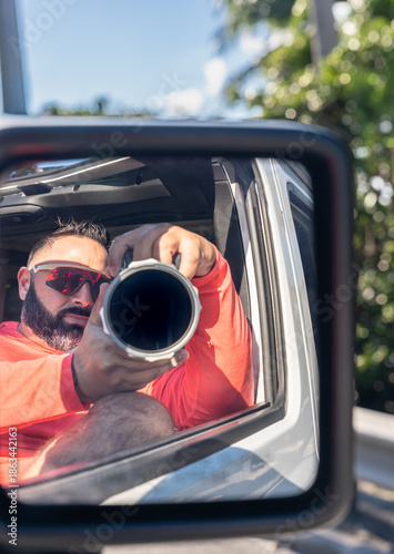 Point-of-view shot of a photographer taking a photo of himself in a car mirror.