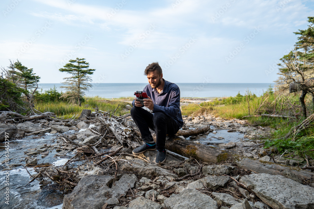 Fototapeta premium A Canadian Man Flies a drone at the Foot of a Waterfall known as “Chute à Boule” in a Forest on Anticosti Island, Quebec, Canada